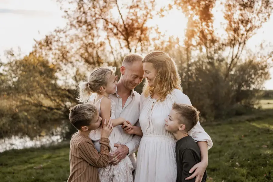 Familie mit drei Kindern am Ufer, alle in Weiß, im herbstlichen Gegenlicht