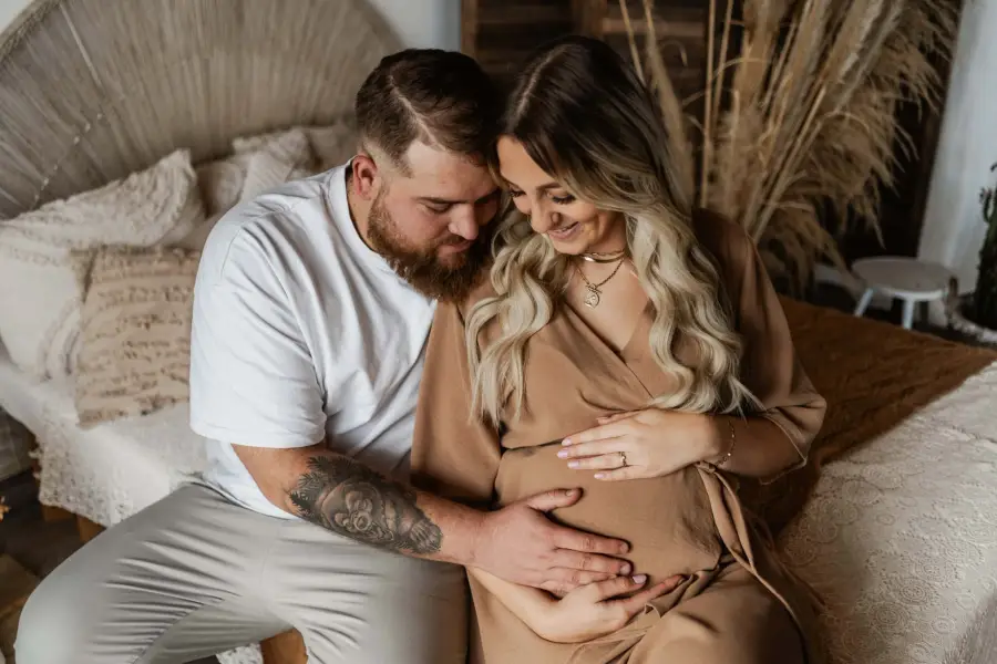 Werdende Eltern auf einem Bett, seine Hände auf ihrem Babybauch