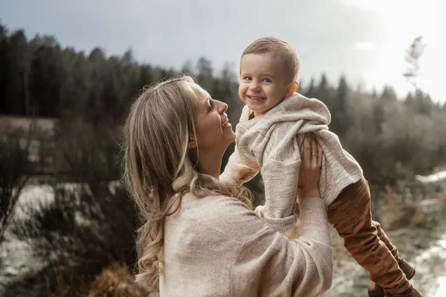 Mutter hebt ihr lachendes Kleinkind hoch, dahinter ein winterliches Feld
