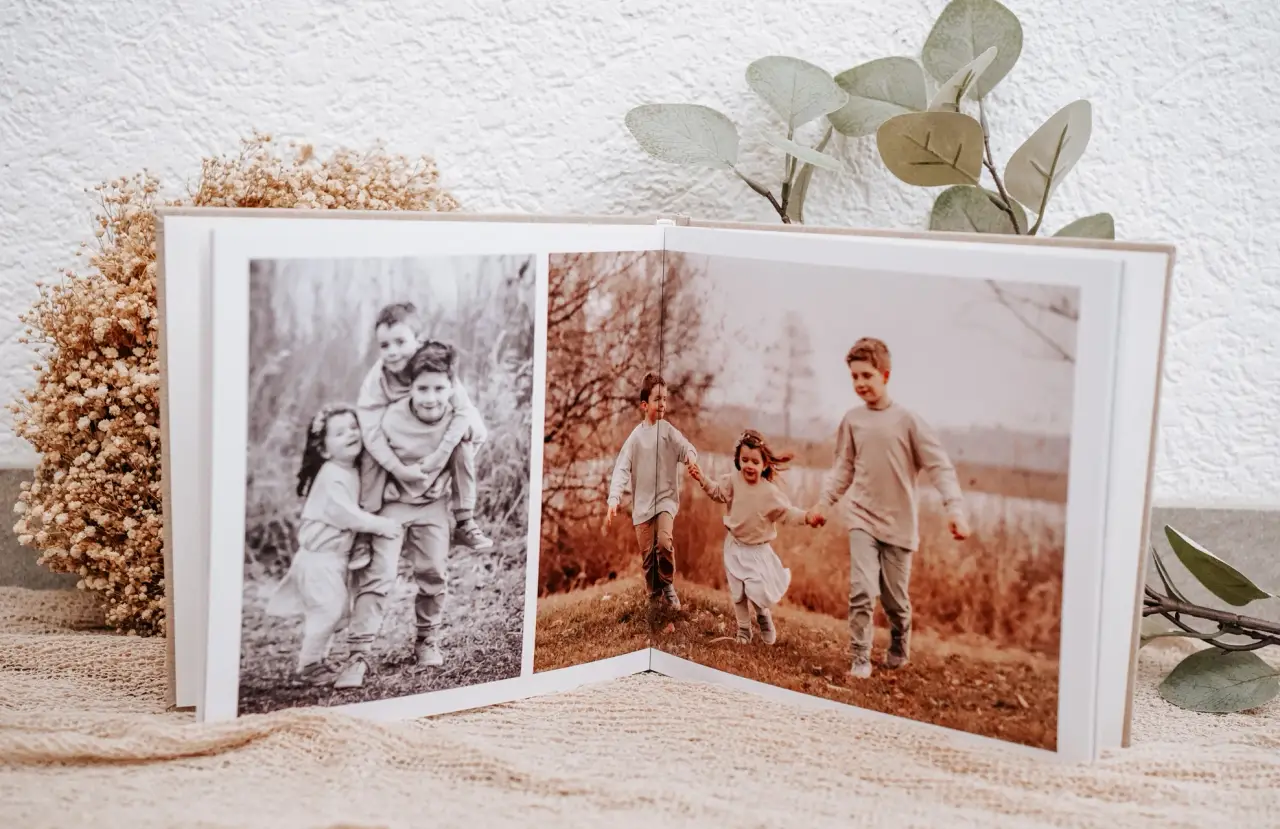 Aufgeschlagenes Fotoalbum: links ein Schwarzweißbild zweier Geschwister, rechts drei Kinder, die Hand in Hand über eine Herbstwiese laufen