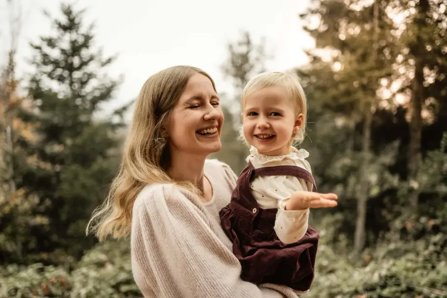 Eine Mutter hält ihr Kleinkind auf dem Arm, beide lachen, das Kind zeigt mit ausgestrecktem Arm in die Ferne
