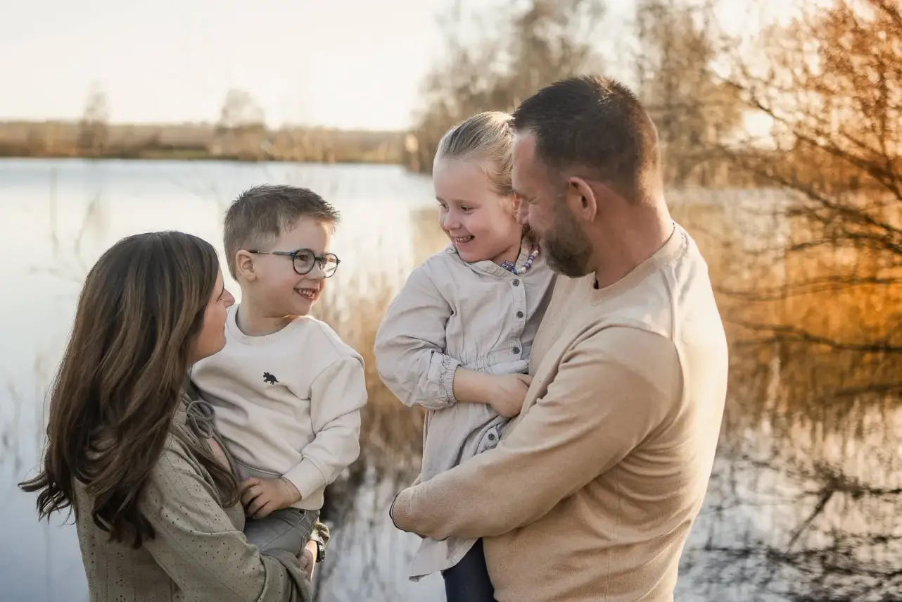 Familie am See im goldenen Abendlicht, die Mama hält den Sohn, der Papa die Tochter, alle lachen