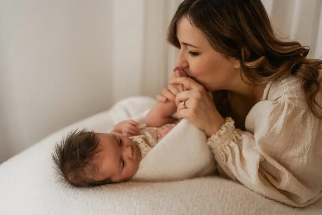 Eine Mutter liegt neben ihrem Neugeborenen und küsst zärtlich seine kleine Hand