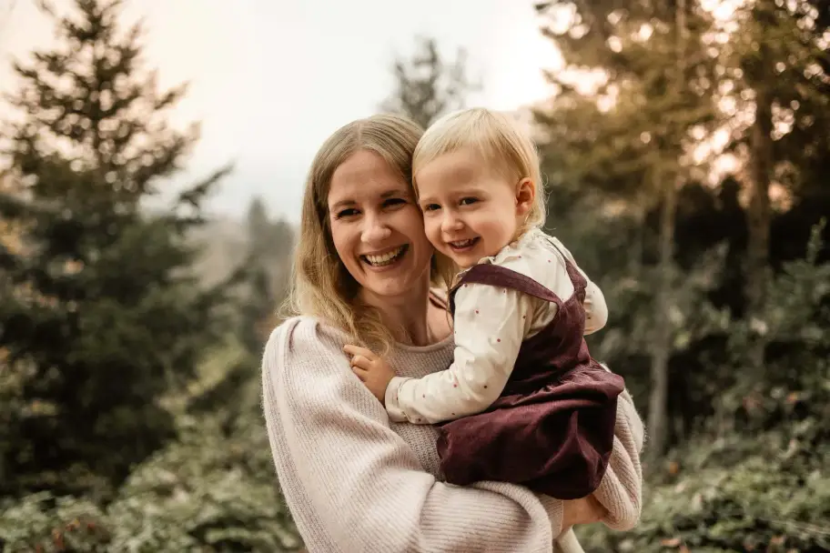 Das Kleinkind schmiegt sich lachend an die Wange seiner Mutter, die mit geschlossenen Augen lacht