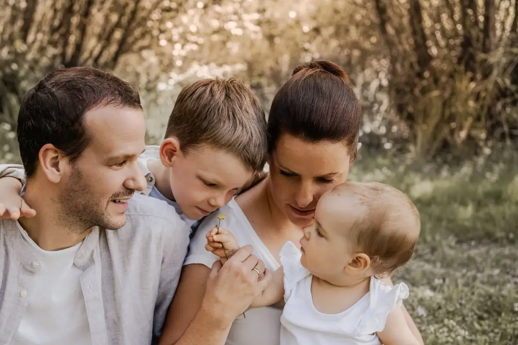 Eine Familie ganz nah beieinander, der Sohn legt die Wange an die Mama, die ihr Baby anlächelt, der Papa schaut zu