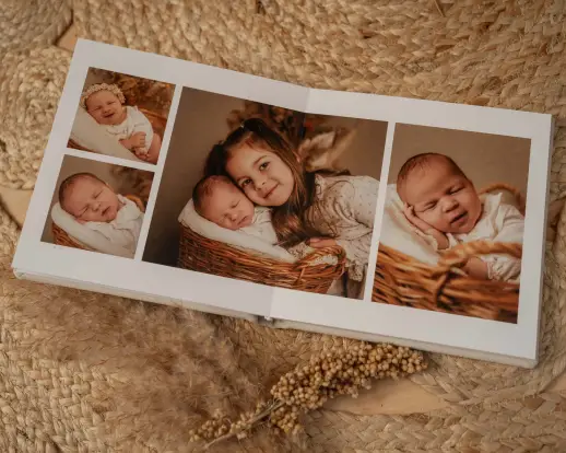 Aufgeschlagenes Fotoalbum mit Babybildern auf einem Juteteppich, daneben Trockengräser