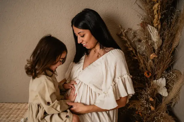 Ein Mädchen legt beide Hände an den Babybauch der Mama, die lächelnd zu ihr hinunterschaut