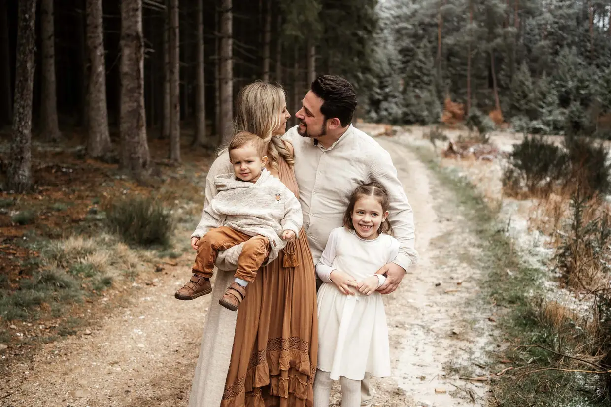 Familie mit zwei kleinen Kindern auf einem Waldweg, die Eltern sehen einander lachend an